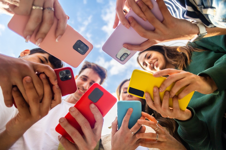 Young group of people using mobile phone device standing in circle outdoors Young group of people using mobile phone device standing in circle outdoors