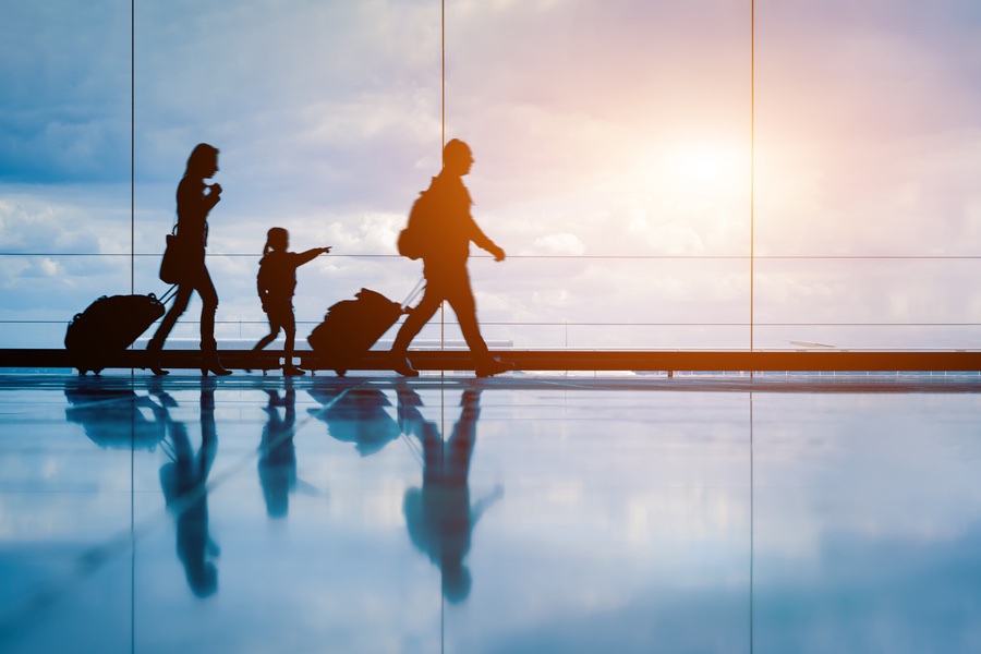 Family at airport travelling with young child and luggage walking to departure gate, girl pointing at airplanes through window, silhouette of people, abstract international air travel concept